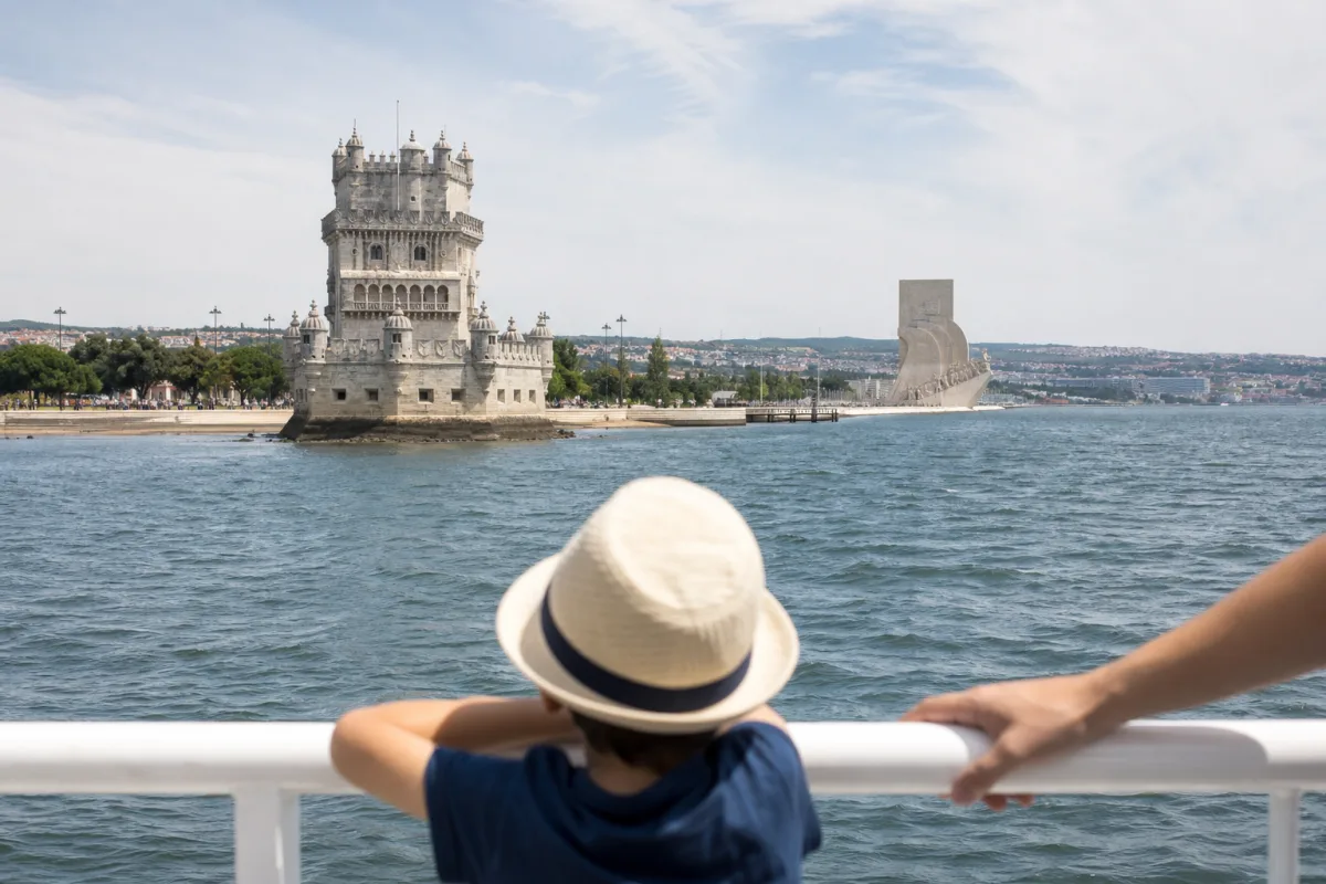 Child at a boat railing on the Tagus looking towards Belém Tower and the Monument to the Discoveries